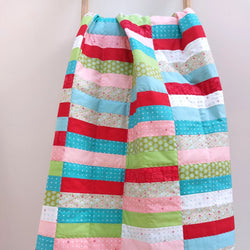 rectangles of fabric sewn together in a coin quilt of red, pink, green, aqua and white