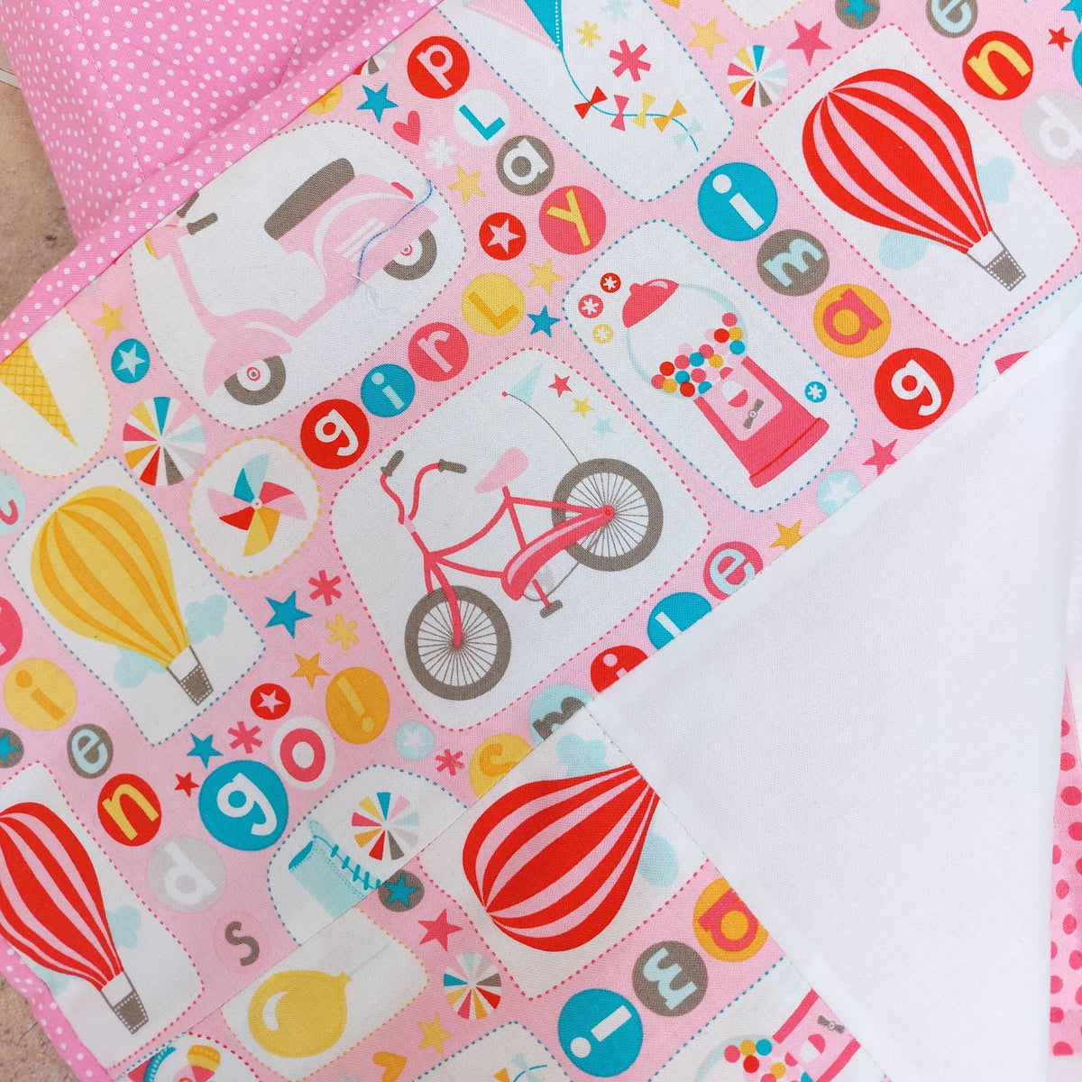 the border of patchwork quilt which includes a bicycle, a pink scooter, hot air balloons and kites