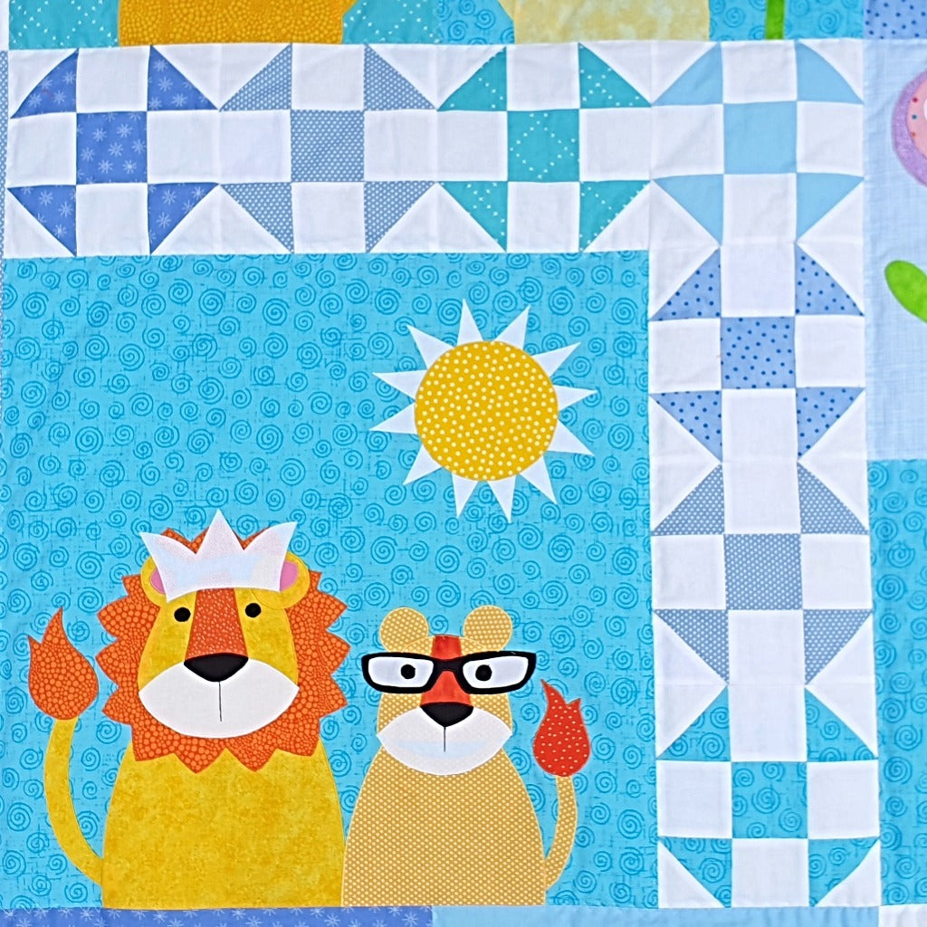 a blue fabric background shows a lion wearing a crown with his  cub and a sun surrounded by a patchwork border of white and different blues 