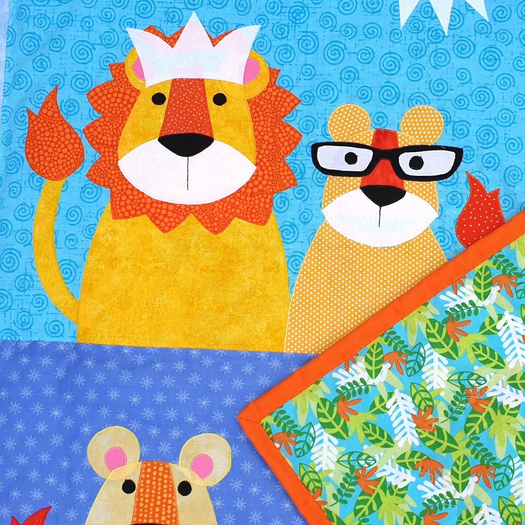a lion wearing a crown and his cub on the front of the quilt with the back showing made of a jungle leaves fabric in blue, white, green and orange