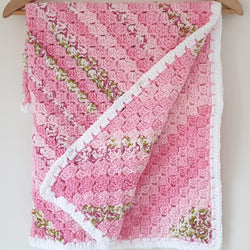 pink and green striped baby blanket with a white border hanging from a coat hanger