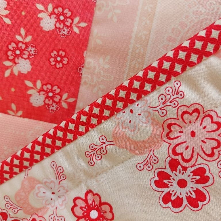 close up of the binding of the quilt with a flower patch in the background