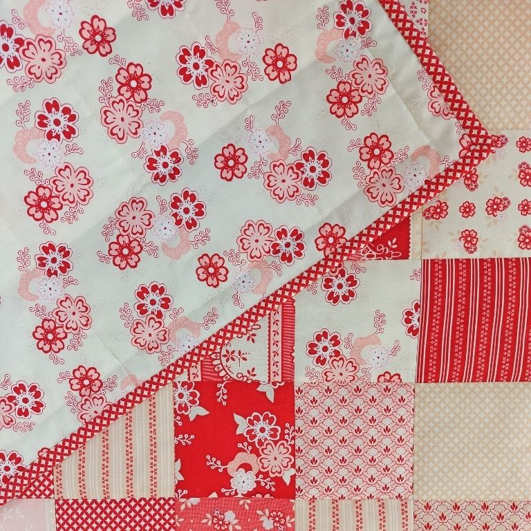 a traditional patchwork quilt made up of squares of raspberry and cream flowers with the backing of raspberry flowers folded over to the front.