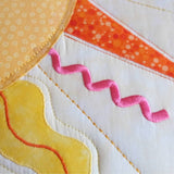 close up view of the suns rays with orange triangle rays, yellow flame rays and pink embroidered pink swirls