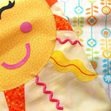 a close up of a smiling sun face with pink cheeks and smile and orange rays. It is folded over to show the quilt back of flowers in orange with green leaves