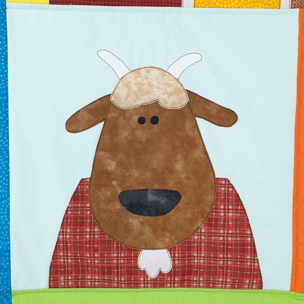 a brown goat on a farm quilt with a white beard and a red check body