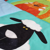 a farm quilt shows a white sheep with black face and an orange cat with white markings and whiskers